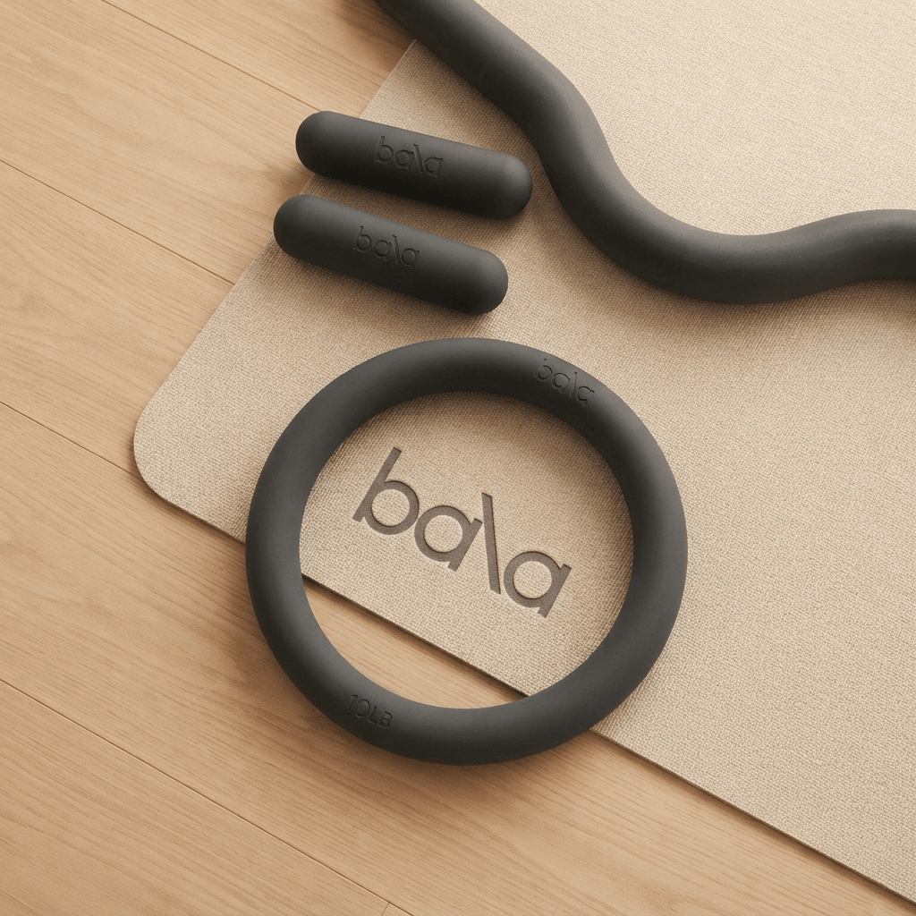 Minimalist Bala pilates equipment including weights and rings on a light-toned floor with soft natural lighting